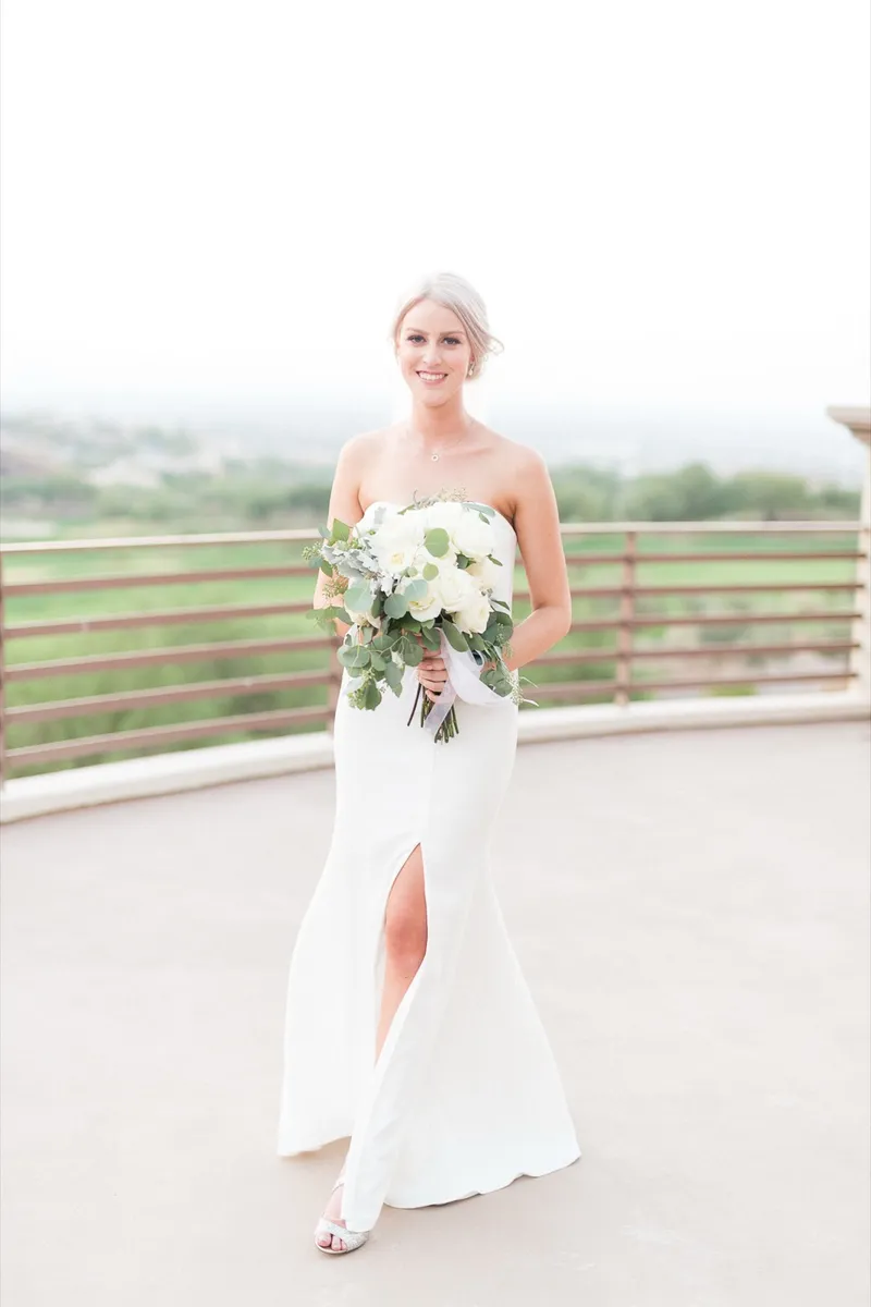Bride standing on the terrace holding her white bouquet, the train of her gown spread at her feet
