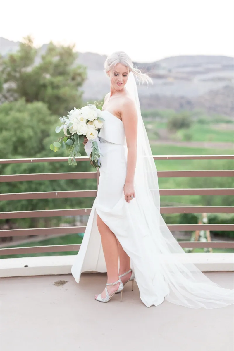 Bride on the terrace with her veil and train trailing behind her along the curve of the wall, hills in the distance