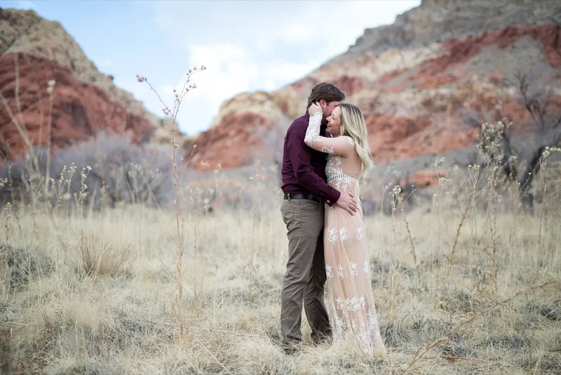 Couple standing forehead to forehead in dry grass with the red and cream canyon walls behind them
