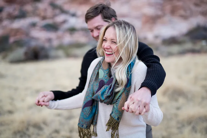 Woman in a teal scarf leading her fiance by both hands through a field of dry desert grass