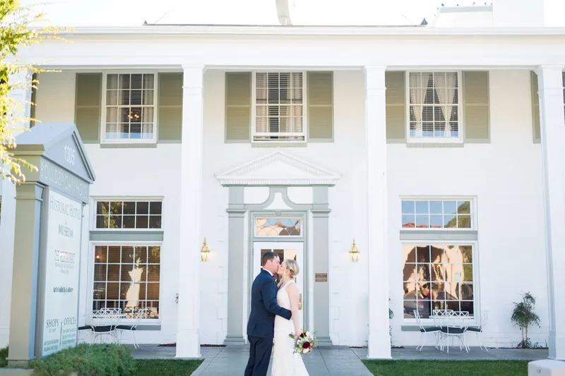 The couple kissing in front of the white columned entrance of the Boulder Dam Hotel, the hotel's blue and white sign standing at the left of the frame