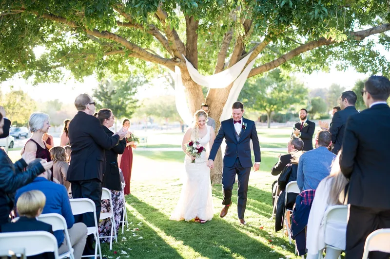 The couple coming back up the aisle after the ceremony, guests turned in their chairs and reaching out as they pass