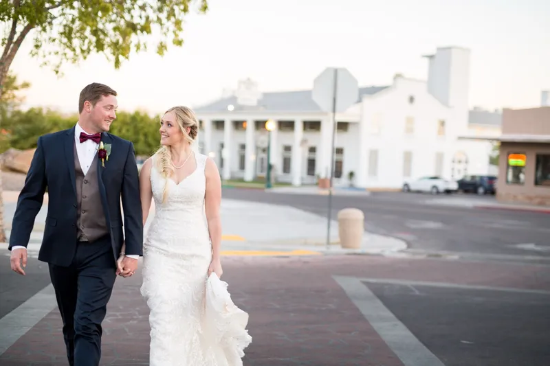 The couple crossing an empty street in the historic district with the white two story hotel and its columns behind them