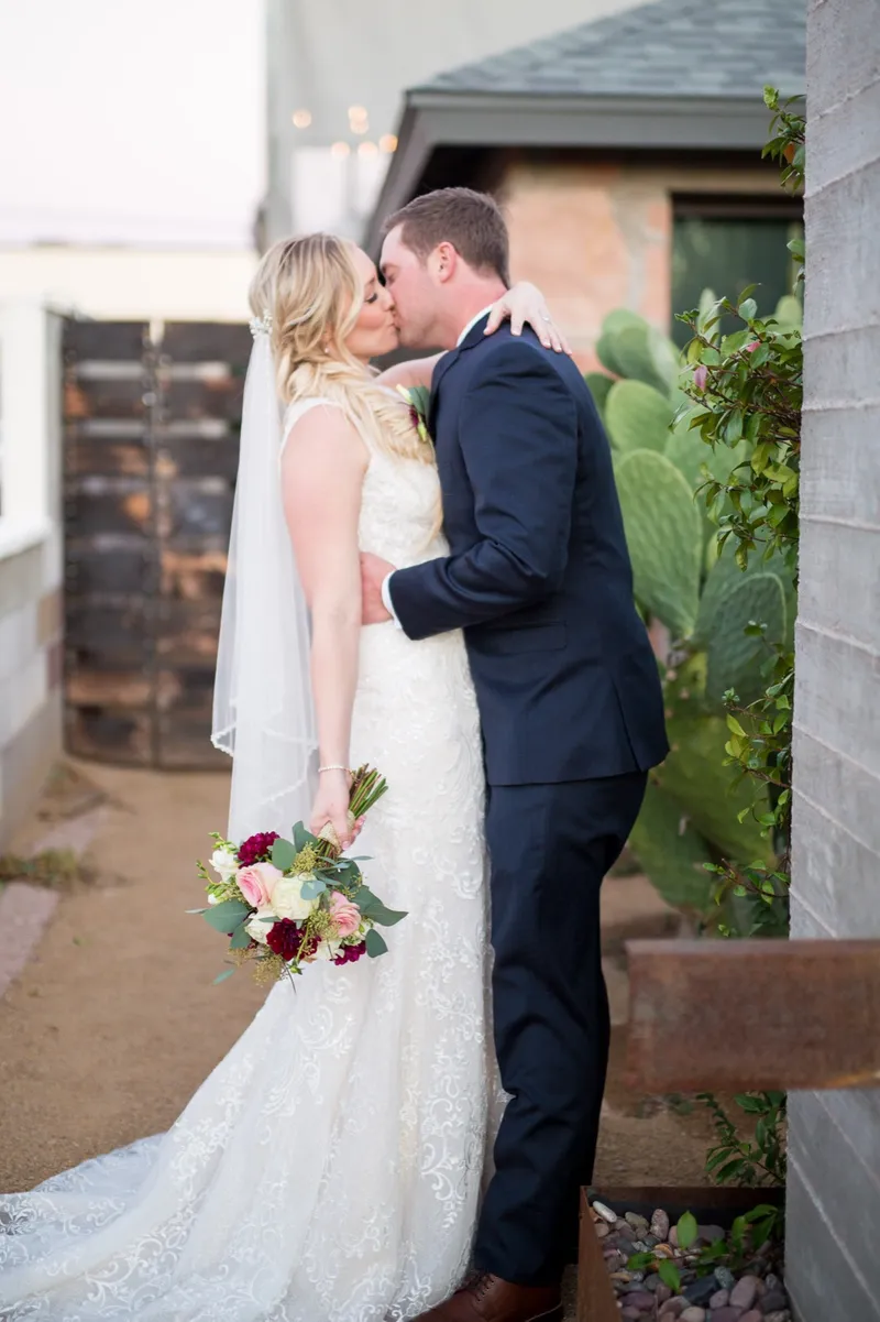 The couple kissing beside the venue's rusted steel gate with prickly pear and bougainvillea growing up the wall next to them