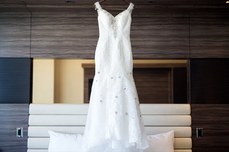 Beaded lace gown hanging against a dark wood wall in the hotel room