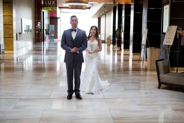 Bride and groom standing side by side on a wide polished marble walkway inside the resort, the corridor running away empty behind them
