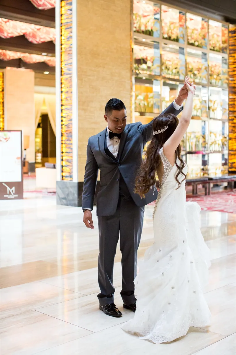 Groom lifting the bride's hand to turn her under his arm on the marble floor, a wall of warm amber panels behind them