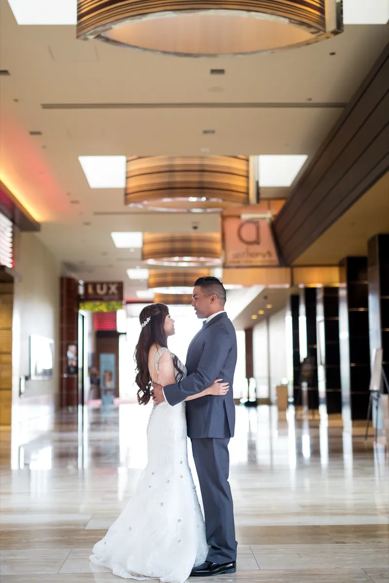 Bride and groom holding each other and looking up, standing alone in the middle of the resort walkway under the drum shaped light fixtures