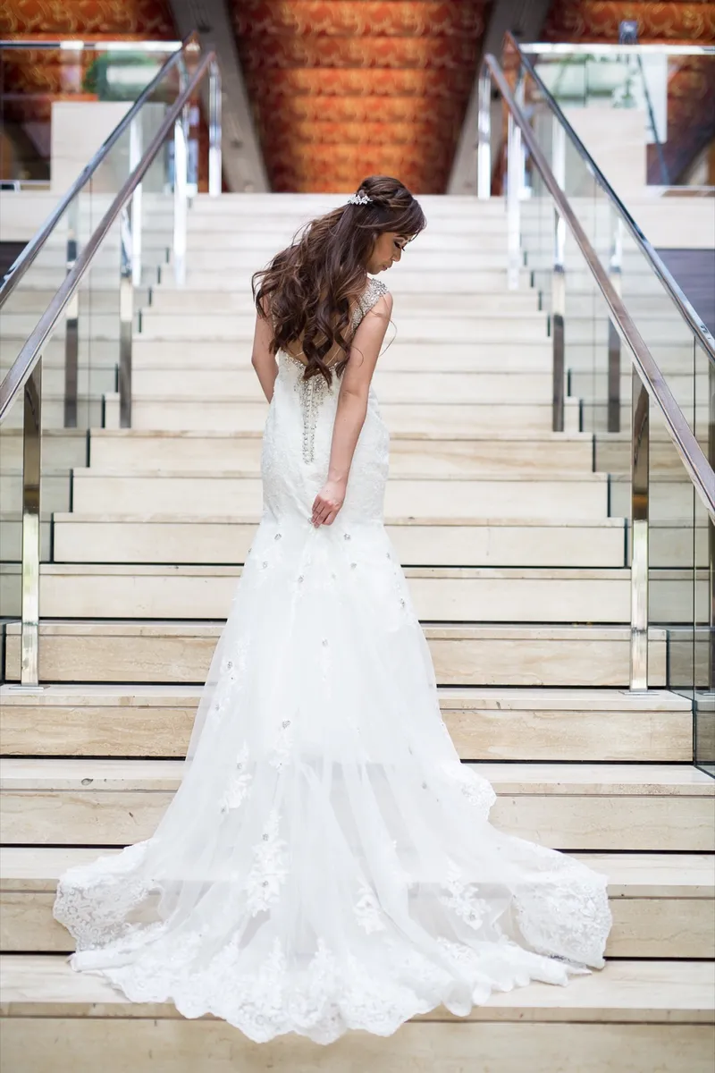 Bride looking back over her shoulder from partway up a wide staircase, her train spilling down the steps behind her