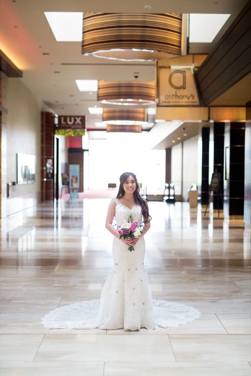 Bride standing alone on the marble walkway holding a bouquet of pink and white roses, her train laid out in front of her