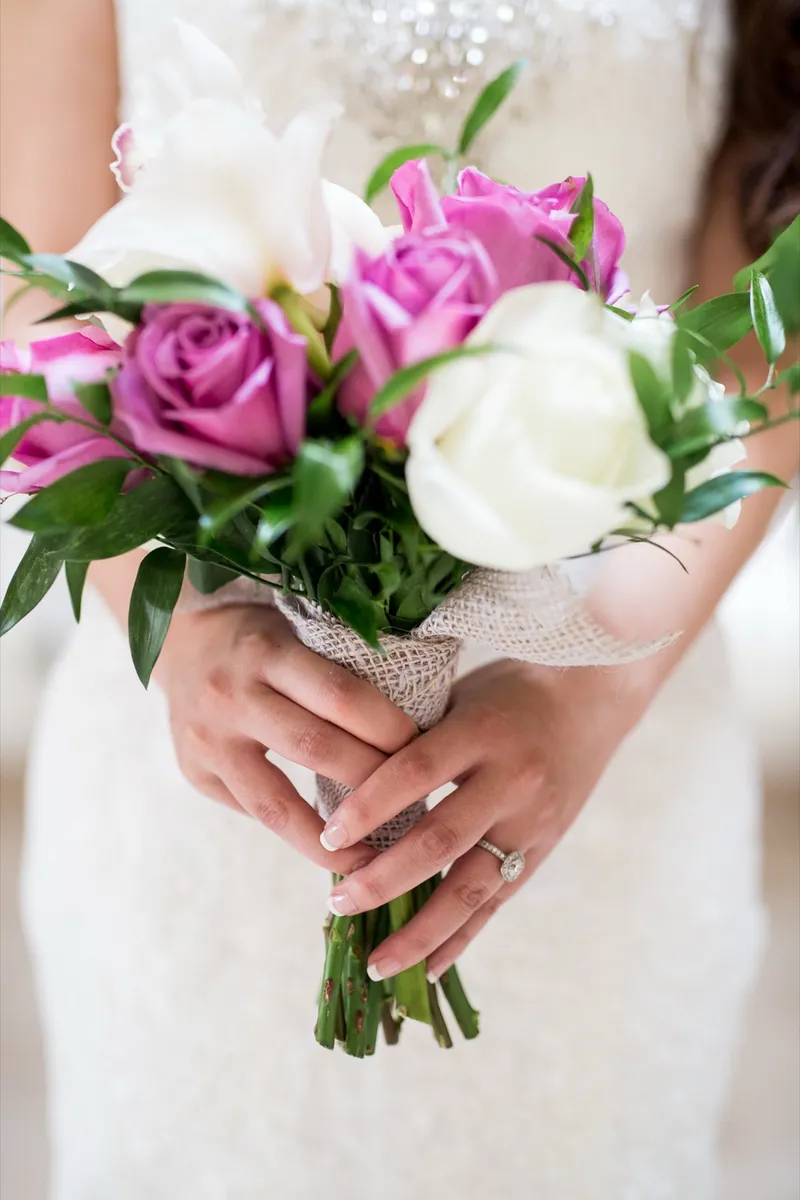 Close view of the bride's hands and her ring resting on the pink and white rose bouquet