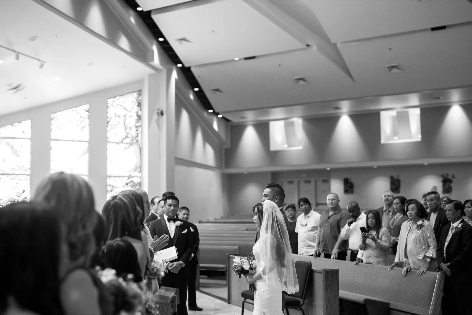 Black and white photo of a groom at the altar watching his bride come up the church aisle