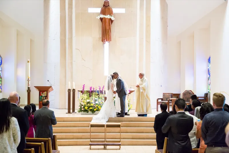 Bride and groom kissing at the top of the altar steps as the priest stands beside them