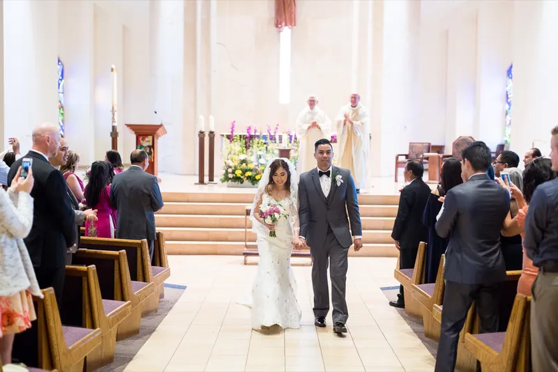 Couple walking back down the aisle after the ceremony while guests lean out of the pews with their phones up