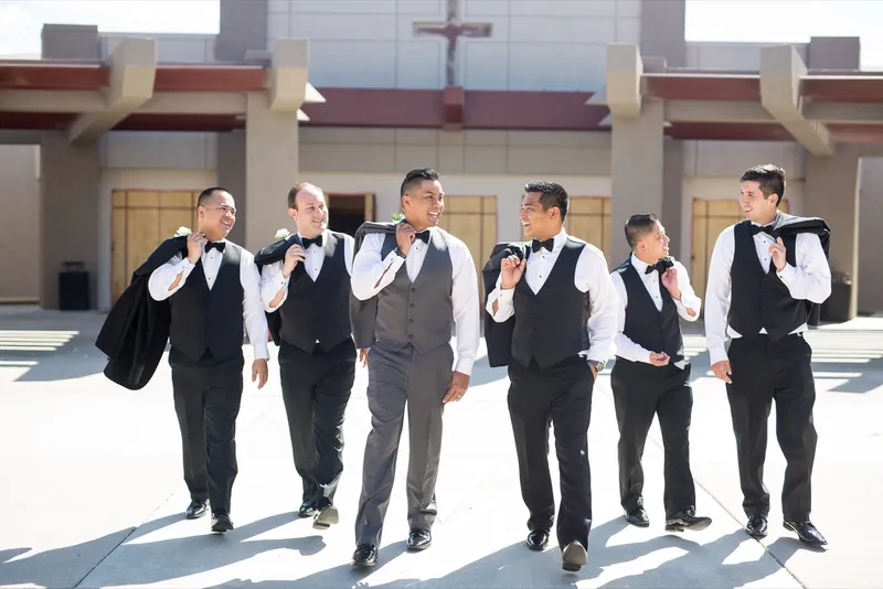 Groom and his groomsmen walking together in front of the church with their jackets slung over their shoulders