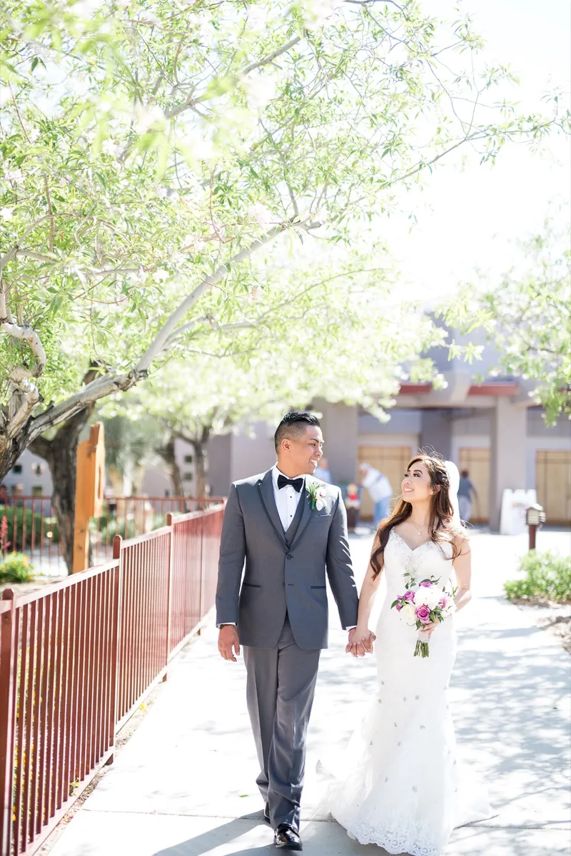 Bride and groom walking hand in hand along the shaded church walkway beside the red railing