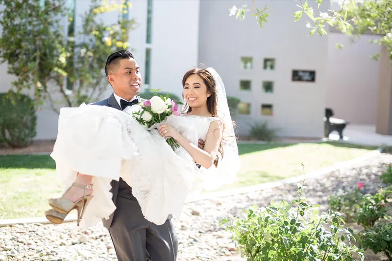 Groom carrying the bride in his arms across the lawn beside the church