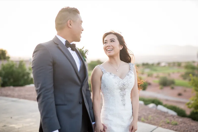Bride and groom walking a paved path and laughing at each other, desert landscaping and the course spread out behind them