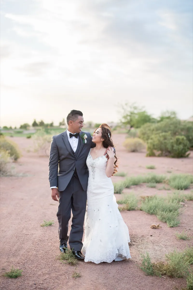 Couple holding each other in the desert brush under a bright blue sky full of broken cloud