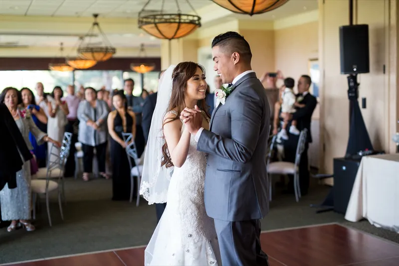First dance on the wooden floor of the clubhouse dining room, the bride still in her veil and the guests watching in a ring around them