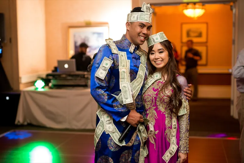 Couple in their ao dai and headpieces standing together draped in leis made of folded dollar bills