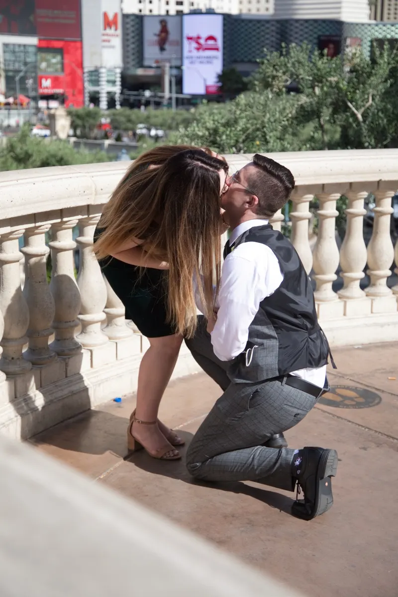 A newly engaged couple kissing on a Bellagio balcony high above the Las Vegas Strip