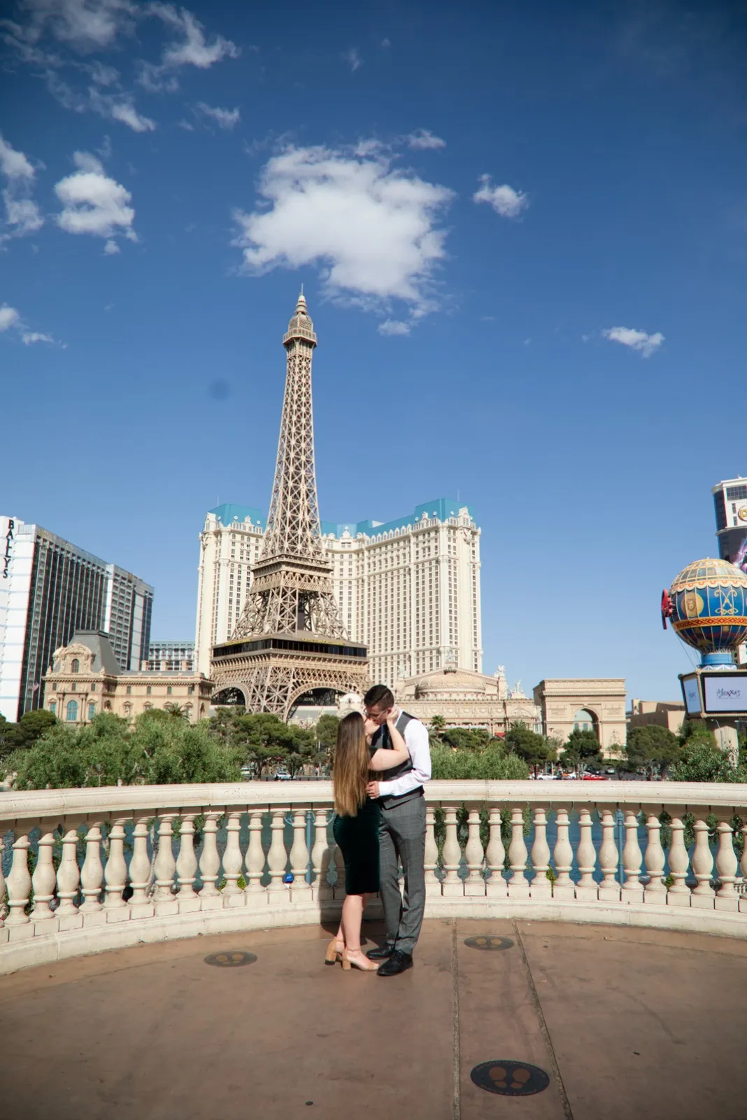 Newly engaged couple kissing on the empty Bellagio overlook, the Eiffel Tower replica rising behind them