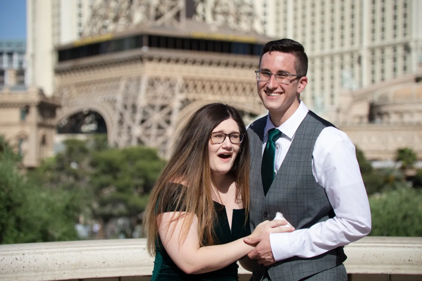 Newly engaged couple holding hands and laughing at the Bellagio fountain overlook, the Paris Las Vegas tower behind them