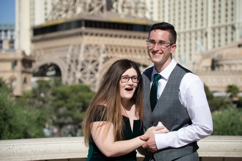 Newly engaged couple holding hands and laughing at the Bellagio fountain overlook, the Paris Las Vegas tower behind them