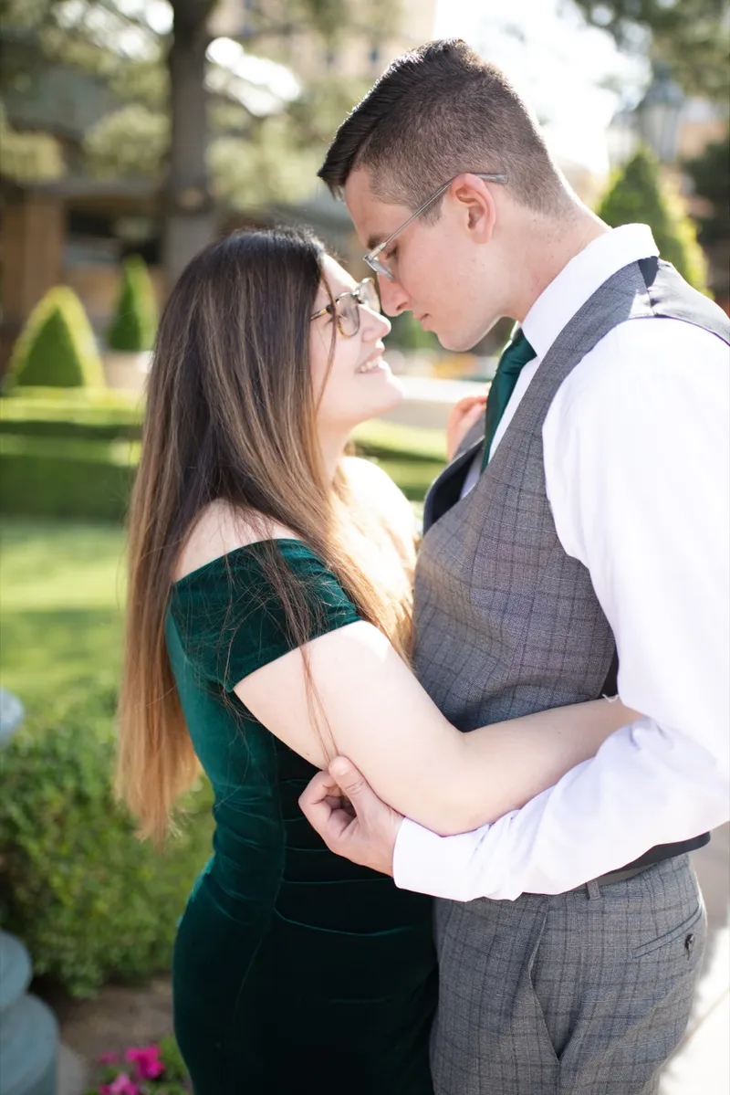 Close photo of the two of them nose to nose, her in a dark green velvet dress and him in a grey vest