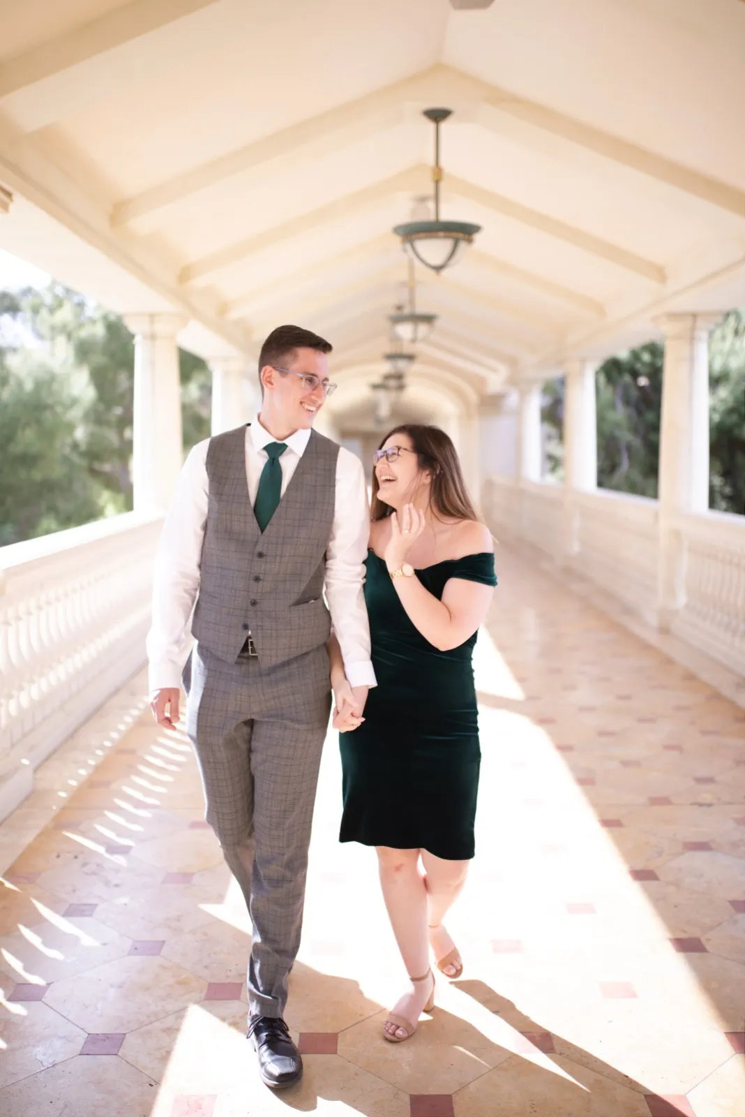 Couple walking hand in hand and laughing down a sunlit covered walkway at the Bellagio