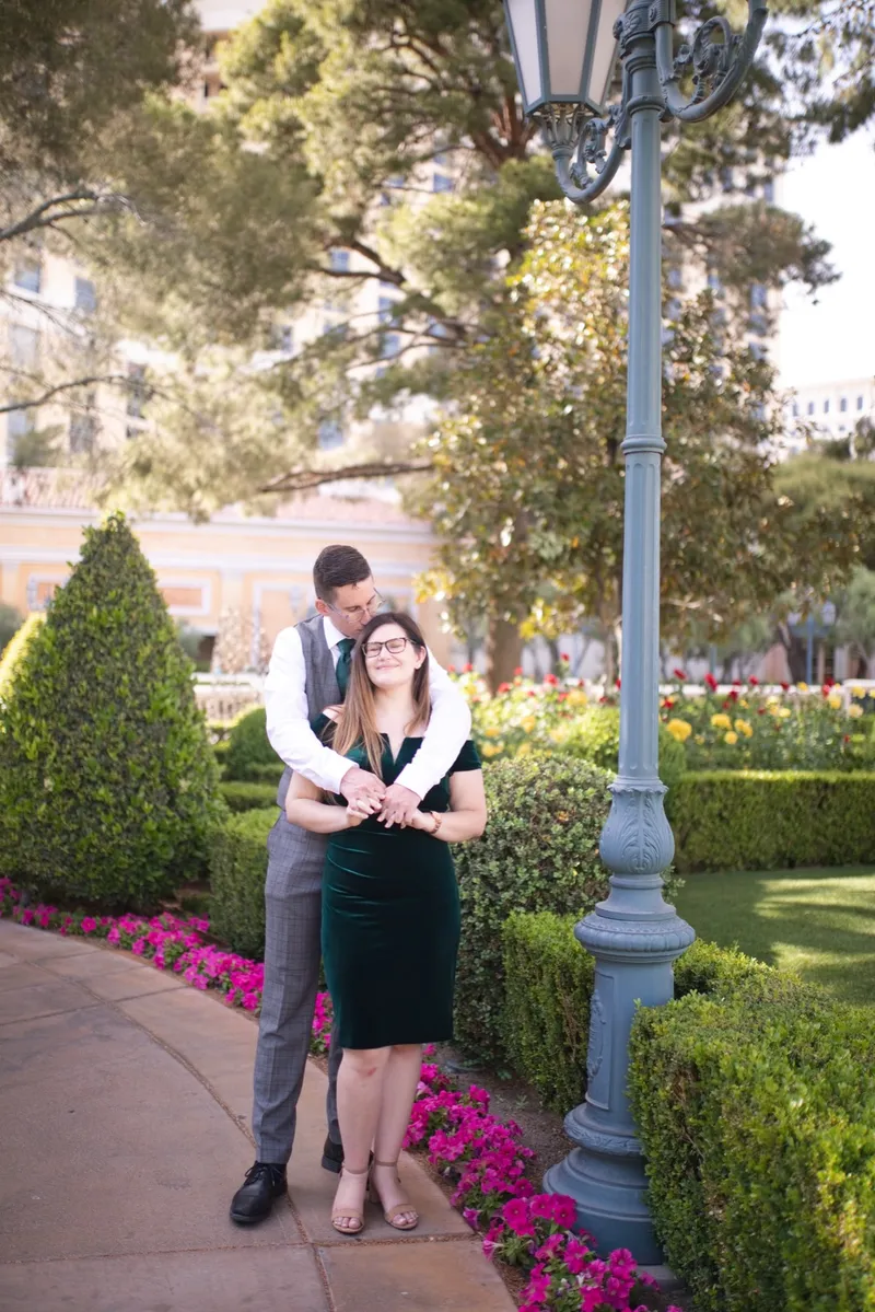 Couple standing together beside a tall lamp post with magenta flowers and low hedges filling the frame