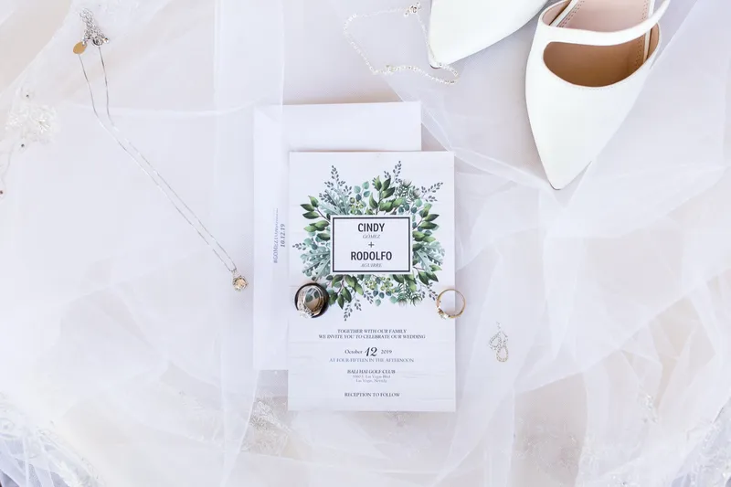 Invitation card, necklace and both rings arranged on the veil beside a pair of white heels