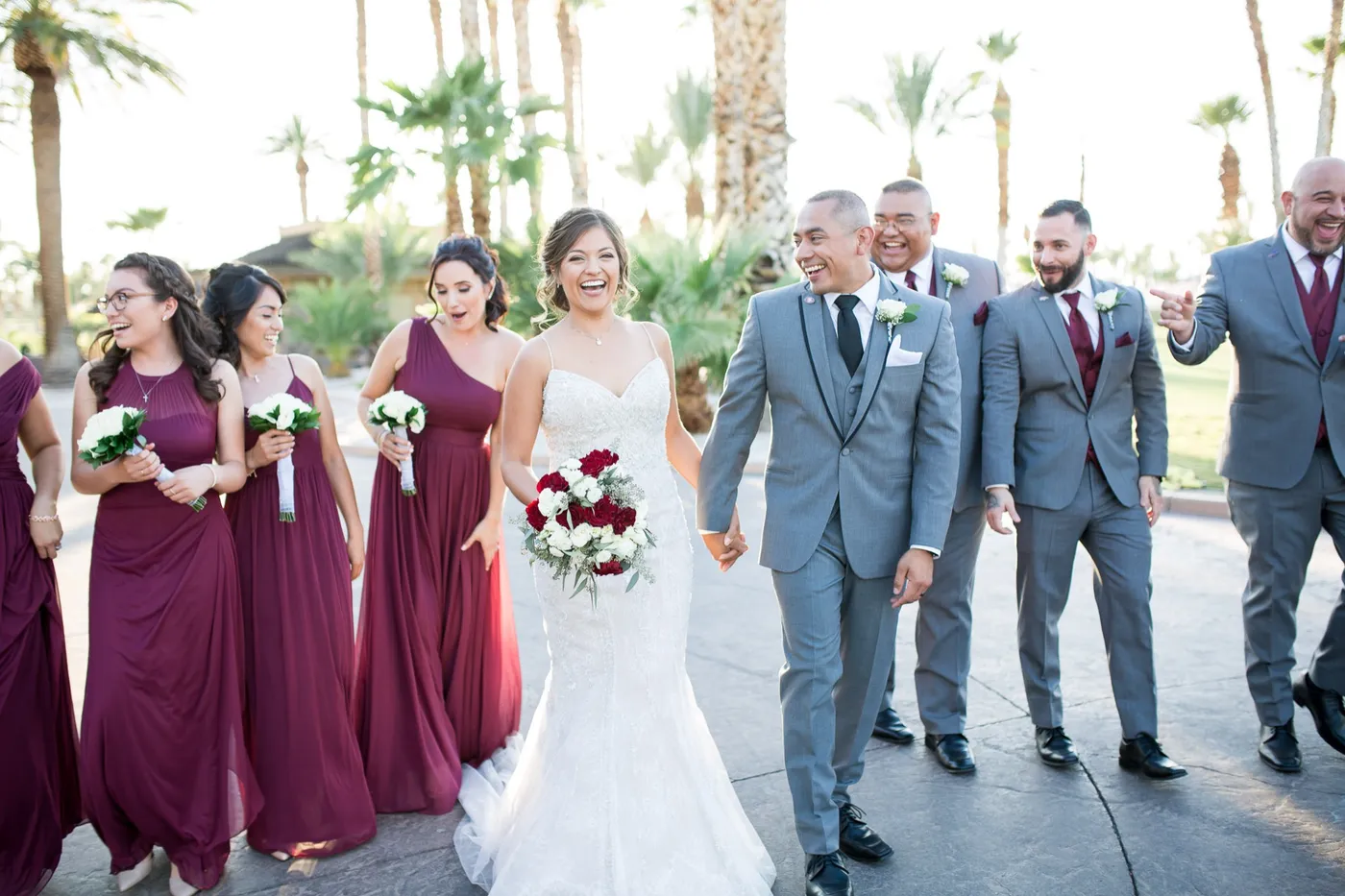 A bride and groom celebrating with their burgundy and gray wedding party under palm trees at a Las Vegas venue