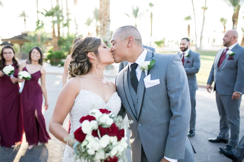 Bride and groom kissing while the wedding party walks and cheers around them