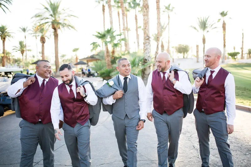 Groomsmen walking the cart path in burgundy vests with their jackets over their shoulders