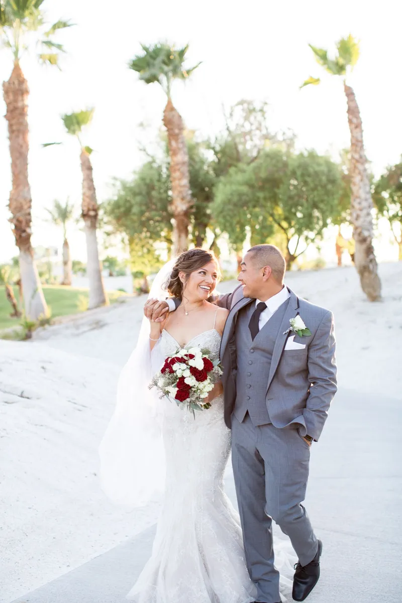 Bride and groom walking hand in hand down the path with palms and the course behind them