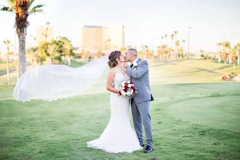 Bride and groom kiss on the fairway, her long veil streaming sideways, the gold Mandalay Bay tower behind them