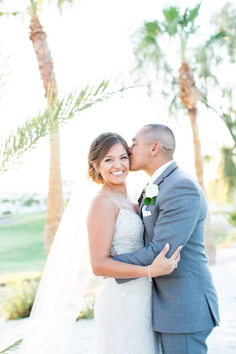 Groom kissing the bride's cheek under backlit palm fronds