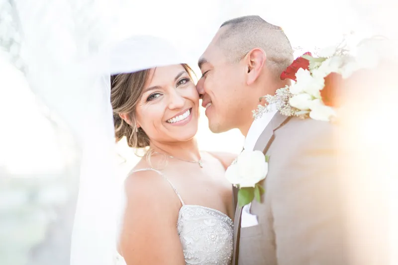 Bride smiling under the veil while the groom leans his forehead against hers