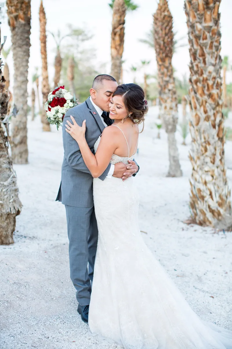 Bride and groom holding each other between two tall palm trunks on the white sand