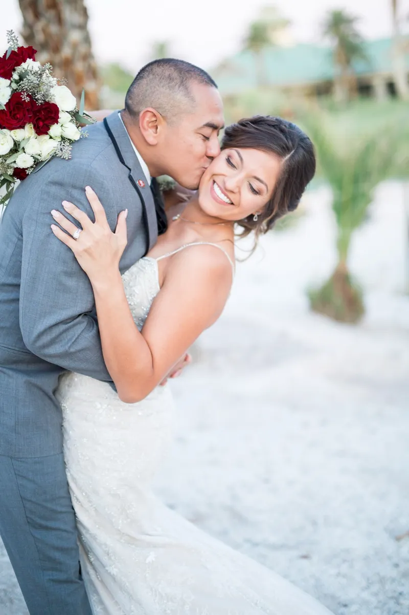 Bride smiling toward the camera while the groom kisses her cheek, the clubhouse roof behind them