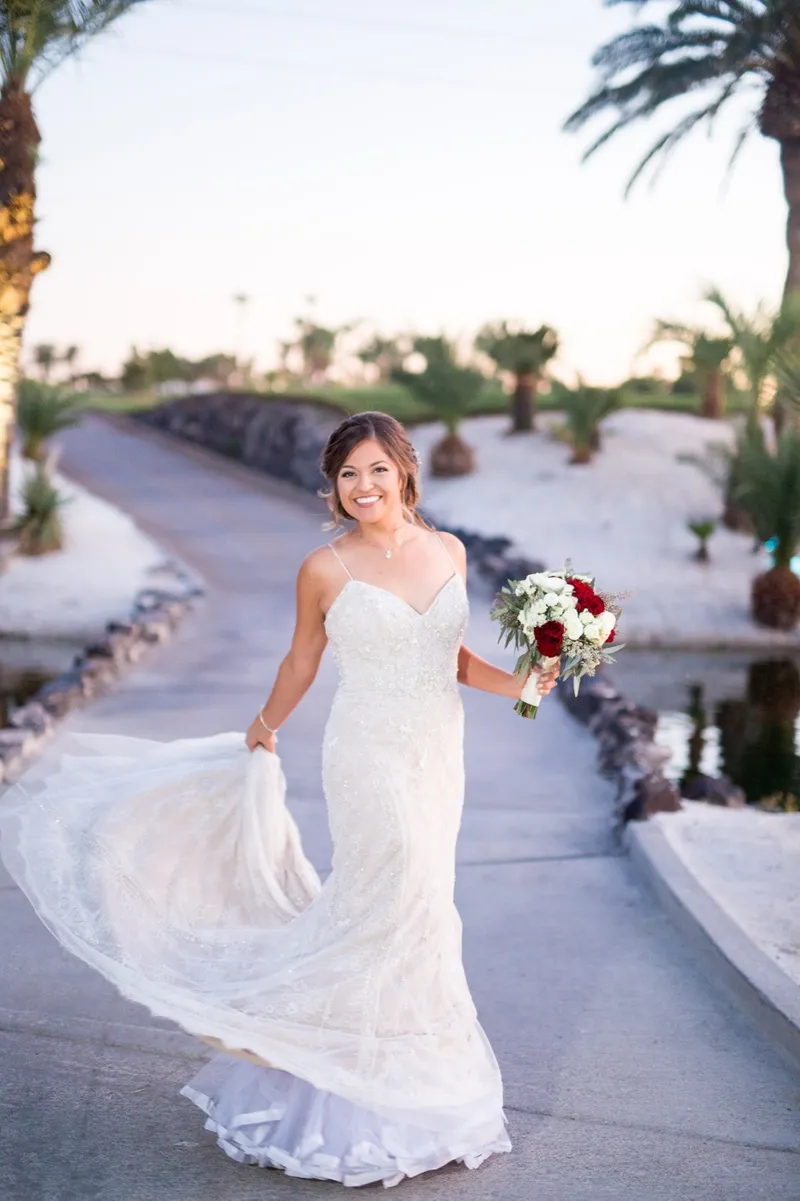 Bride sweeping her train along the path at sunset with her bouquet in one hand