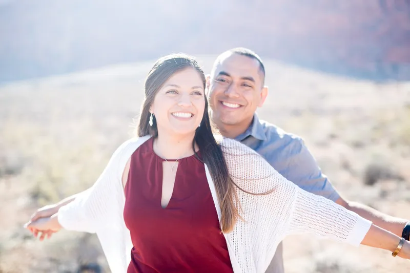Couple throwing their arms out wide and laughing with the low sun behind them
