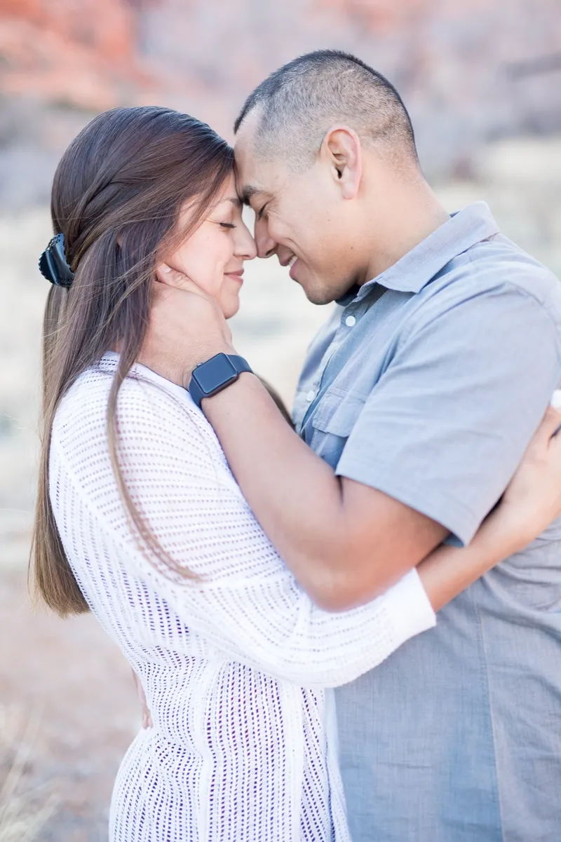 Couple standing forehead to forehead with her arms around his neck and a white knit sweater on her shoulders