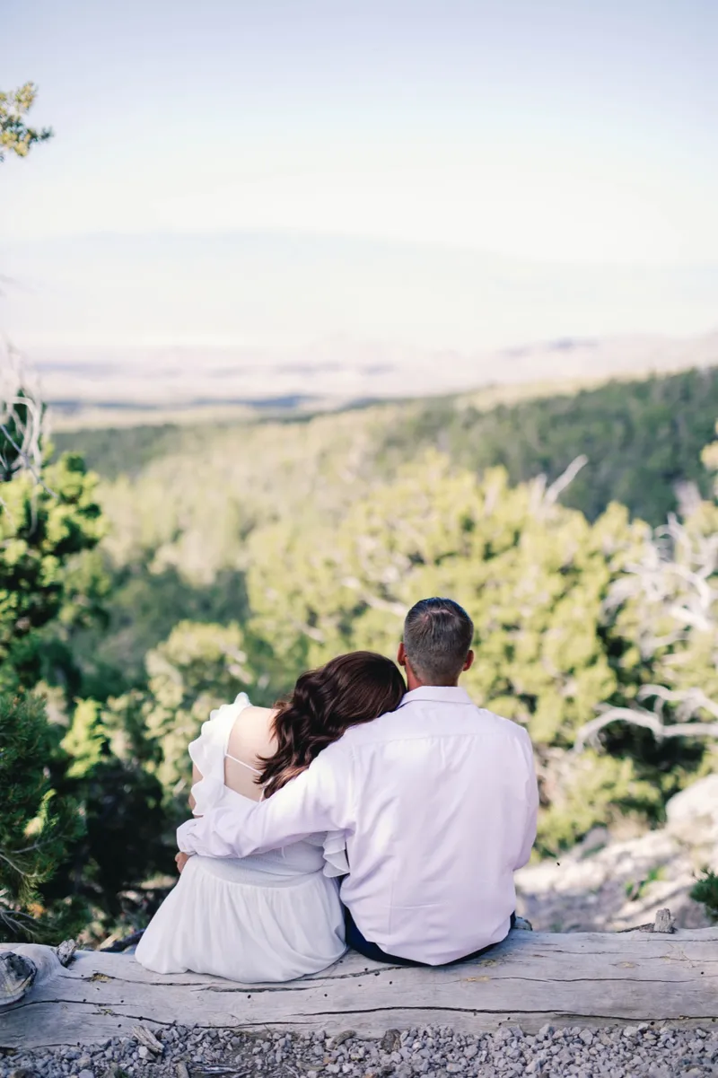 Couple sitting close on a fallen log at the edge of an overlook, her head resting on his shoulder