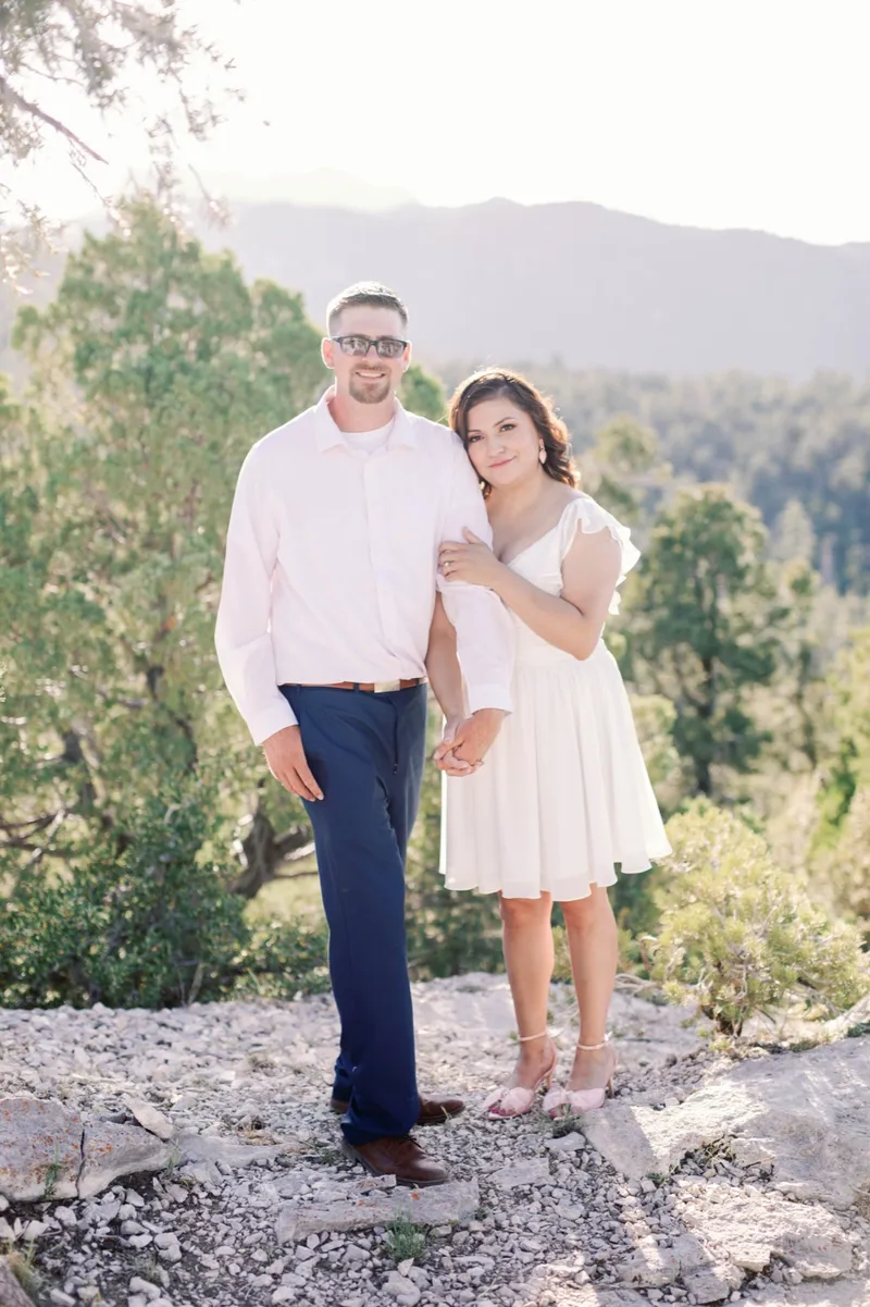 Man in a pale pink shirt standing on a limestone ledge with his fiancee tucked in beside him