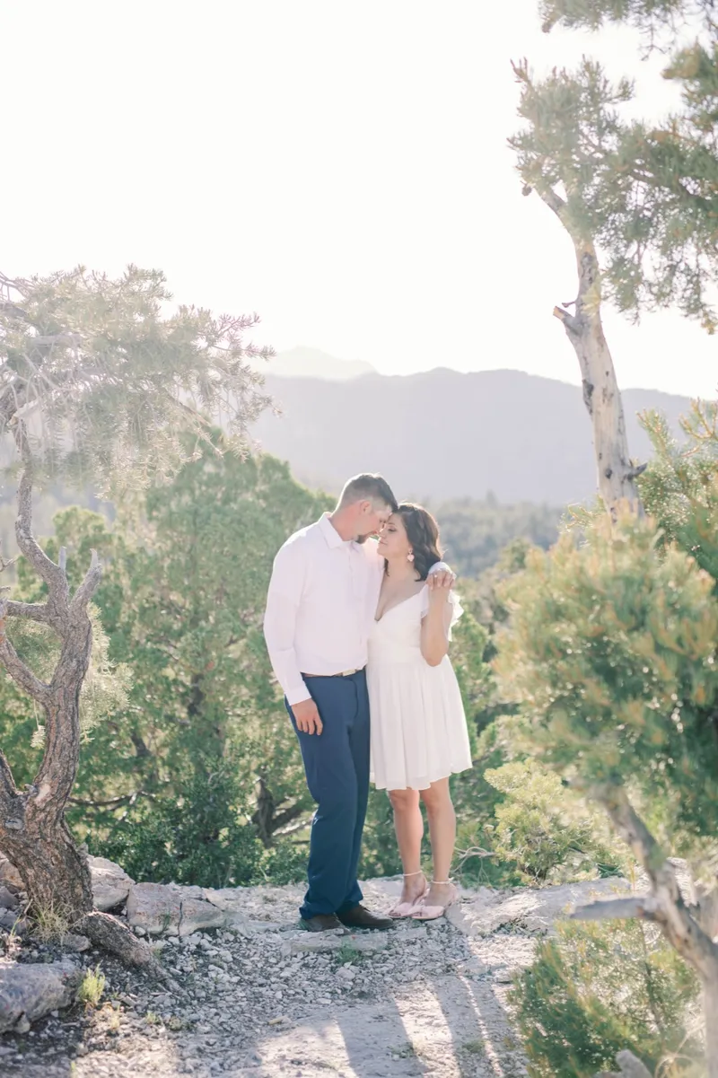Couple standing forehead to forehead on a rocky trail with a hazy ridge behind them
