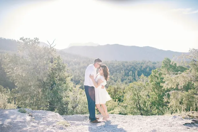 Couple standing close together on a limestone overlook with pine covered slopes and a hazy ridge behind them