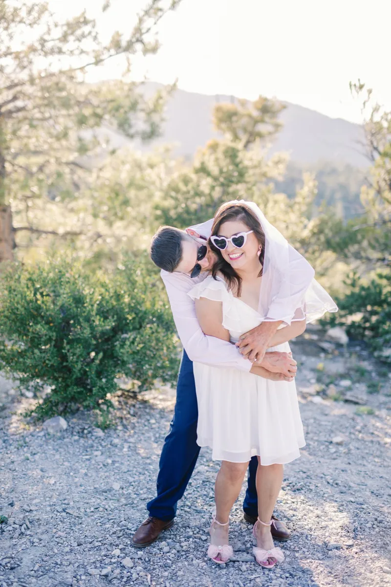 Couple in sunglasses laughing together on the mountainside with her veil floating out behind her